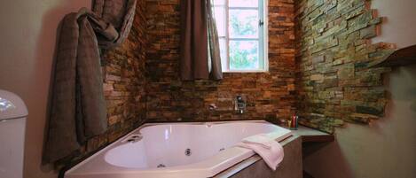 Ein Badezimmer mit Steinwand, Fenster, Badewanne und einem Handtuch an der Wand.