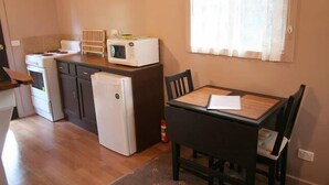 Cocina compacta con estufa, microondas y refrigerador. Hay una mesa de comedor con sillas y una ventana con cortinas.