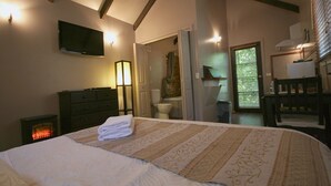 Un dormitorio con una cama grande, una chimenea, un televisor y un baño visible a través de una puerta abierta.
