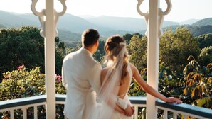 Una pareja está de pie en un quiosco con vistas panorámicas a montañas y vegetación.