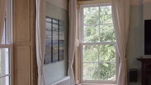 Ein Zimmer mit einem dunkelbraunen Ledersofa, einem fenster mit Vorhängen, einem Heizkörper und einem Wandlautsprecher.