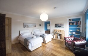 Un dormitorio con dos camas, chimenea, estantería y un sillón de cuero.