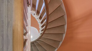 Eine Wendeltreppe mit hölzernen Geländern und beigen Stufen vor einer orangefarbenen Wand.