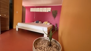A bedroom with a bed, a wooden floor, a pink wall, and a window with a curtain. - Charming Poolside Studio with Private Porch in Curaçao (Willemstad)