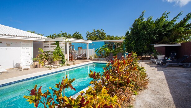 A swimming pool with a covered area, lounge chairs, and a small garden. - Charming Poolside Studio with Private Porch in Curaçao (Willemstad)