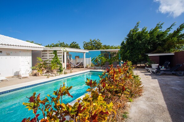A swimming pool with a covered area, lounge chairs, and a small garden.
