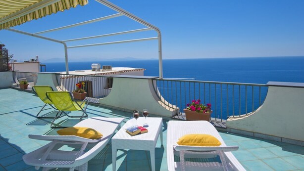 Un balcone con poltrone da relax bianche, un tavolino con bevande e piante in vaso.
