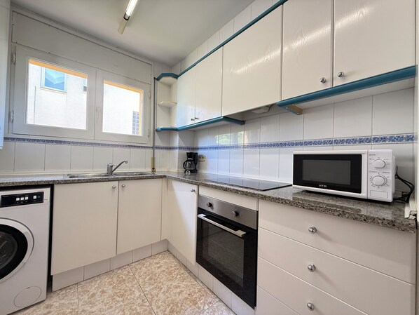 A compact kitchen with white cabinets, a microwave, a coffee maker, and a dishwasher.