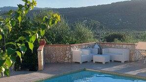 Un espace piscine agrémenté d’un mur en pierre, de chaises longues et d’une table sur laquelle se trouve un panier tressé et des objets décoratifs.