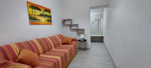 A room with a striped sofa, a small table, a painting, and a bathroom door.