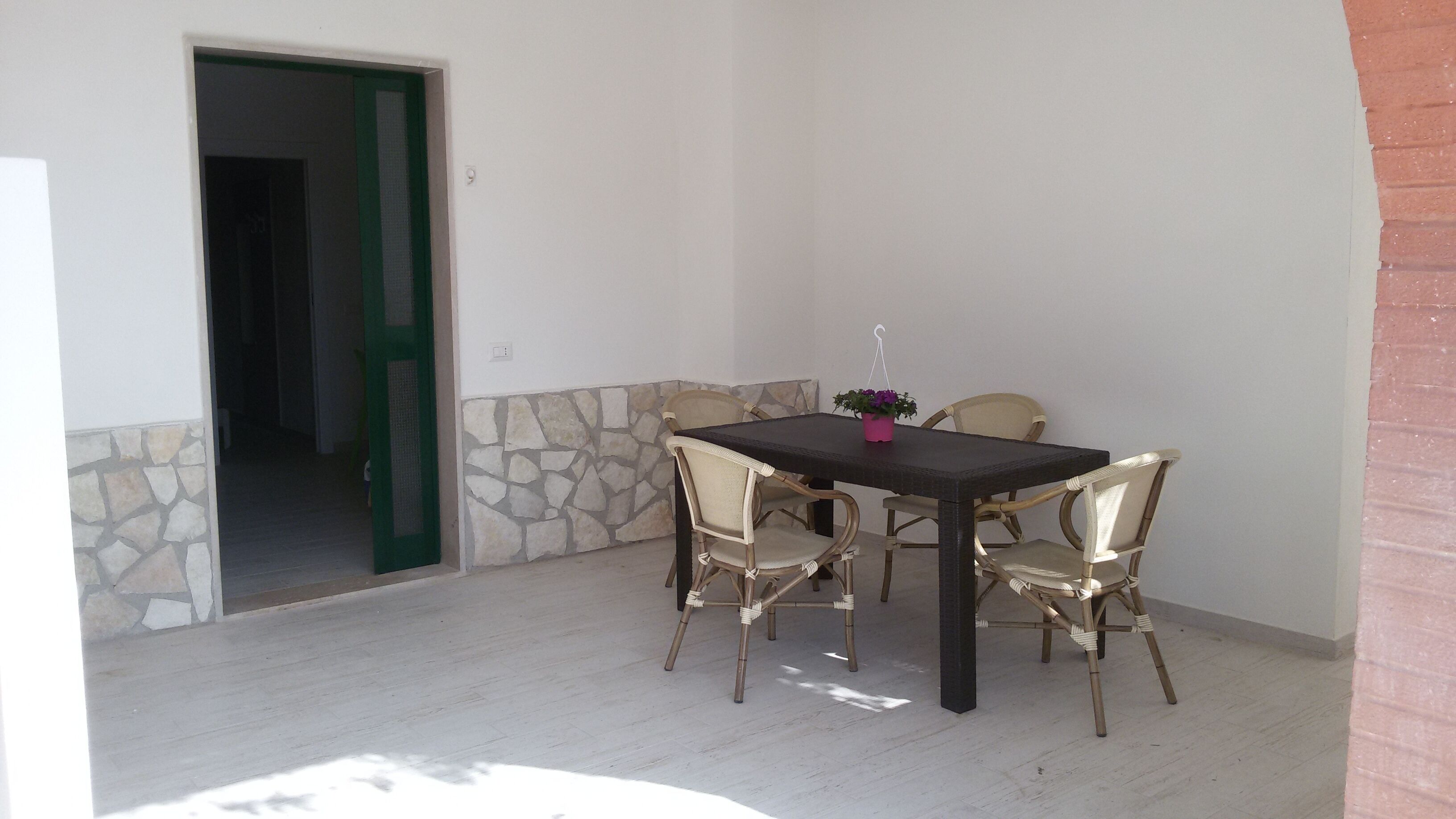Un coin repas avec une table et quatre chaises, une plante en pot et un mur en pierre.