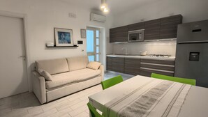 Une cuisine moderne équipée d’un four à micro-ondes encastré, d’une cuisinière à gaz et d’un réfrigérateur. On y trouve également un canapé beige et une table à manger avec des chaises.