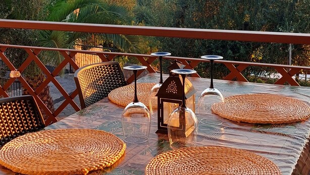 Un espace de restauration en plein air avec une table dressée pour quatre personnes, entourée de chaises en osier, et offrant une vue sur un paysage pittoresque.