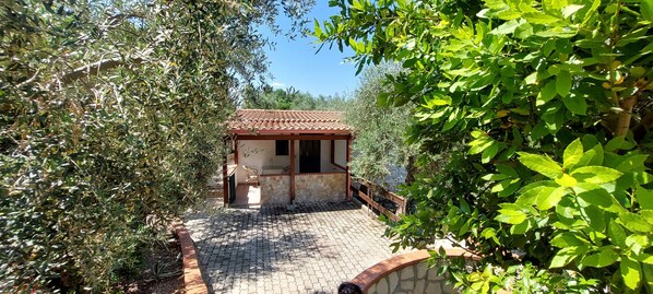 Un petit bâtiment rustique, doté d’un toit en tuiles et d’un mur en pierre, entouré d’une végétation luxuriante.