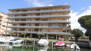 A multi-story building with balconies, a marina with boats, and a clear sky.