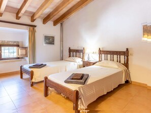 A bedroom with two wooden beds, a window with curtains, a wall-mounted picture, and a bedside table with a lamp. - Ca Na Bassera, Country house in Alcudia, Mallorca (Alcúdia)