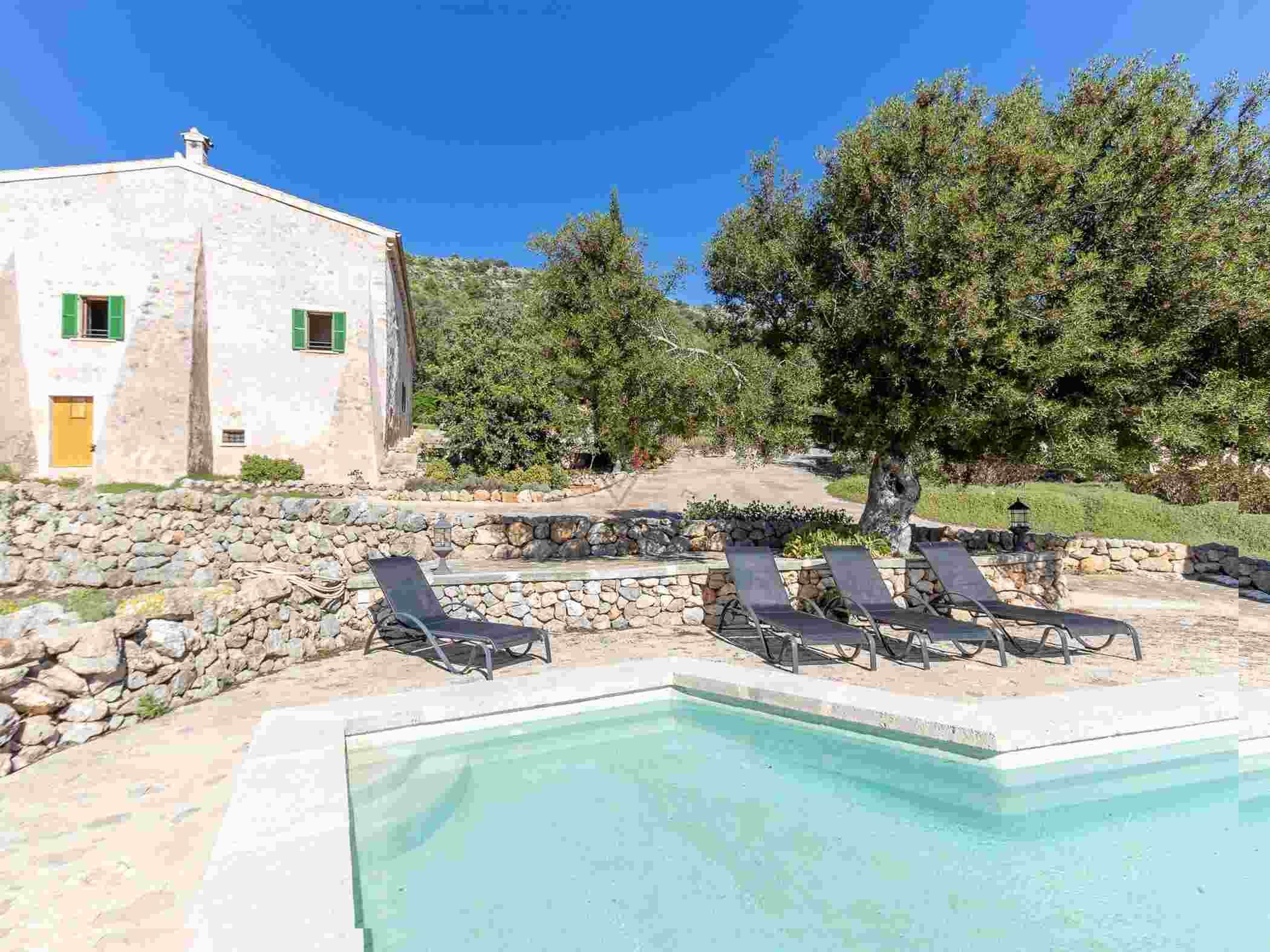 A pool area with lounge chairs and a stone wall.