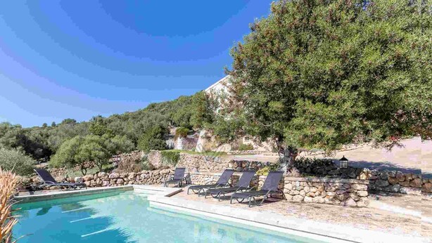 A swimming pool with lounge chairs, surrounded by stone walls and trees. - Ca Na Bassera, Country house in Alcudia, Mallorca (Alcúdia)