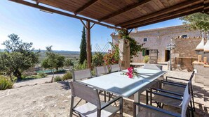 An outdoor patio with a table and chairs, a pergola overhead, and a view of a stone building and landscape. - Ca Na Bassera, Country house in Alcudia, Mallorca (Alcúdia)