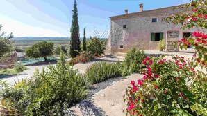 A rustic stone building with a garden, a clear sky, and a distant view of the countryside. - Ca Na Bassera, Country house in Alcudia, Mallorca (Alcúdia)