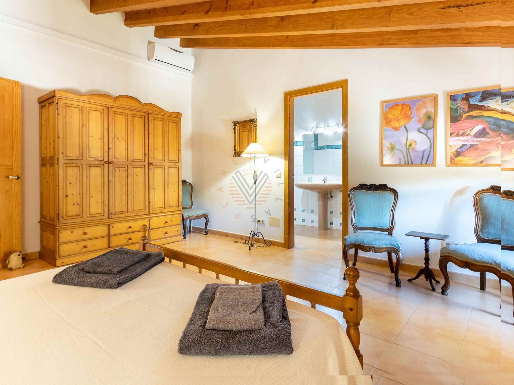 Una habitación con un armario de madera, un espejo, una lámpara, un lavamanos y dos sillas.