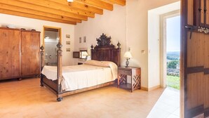 A bedroom with a wooden bed, a ceiling fan, a wooden wardrobe, and a view of the outside. - Ca Na Bassera, Country house in Alcudia, Mallorca (Alcúdia)