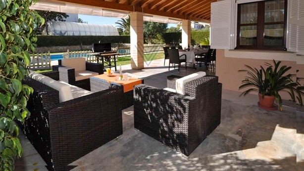 Pátio externo com móveis de vime, piscina e área coberta com teto de madeira.