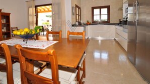 Uma cozinha moderna com uma geladeira de aço inoxidável grande, uma mesa de jantar com cadeiras e uma ilha central com pia.