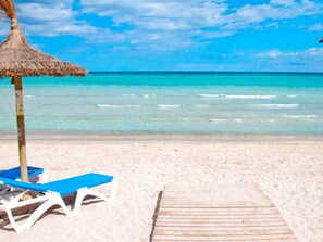 A beach with a thatched umbrella, a wooden walkway, and a blue lounge chair.