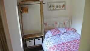 Un dormitorio con una cama, un estante de madera con cestas, un perchero y un cuadro colgado en la pared.
