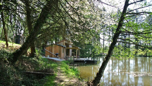 Una cabaña de madera junto a un lago con un muelle, rodeada de árboles.