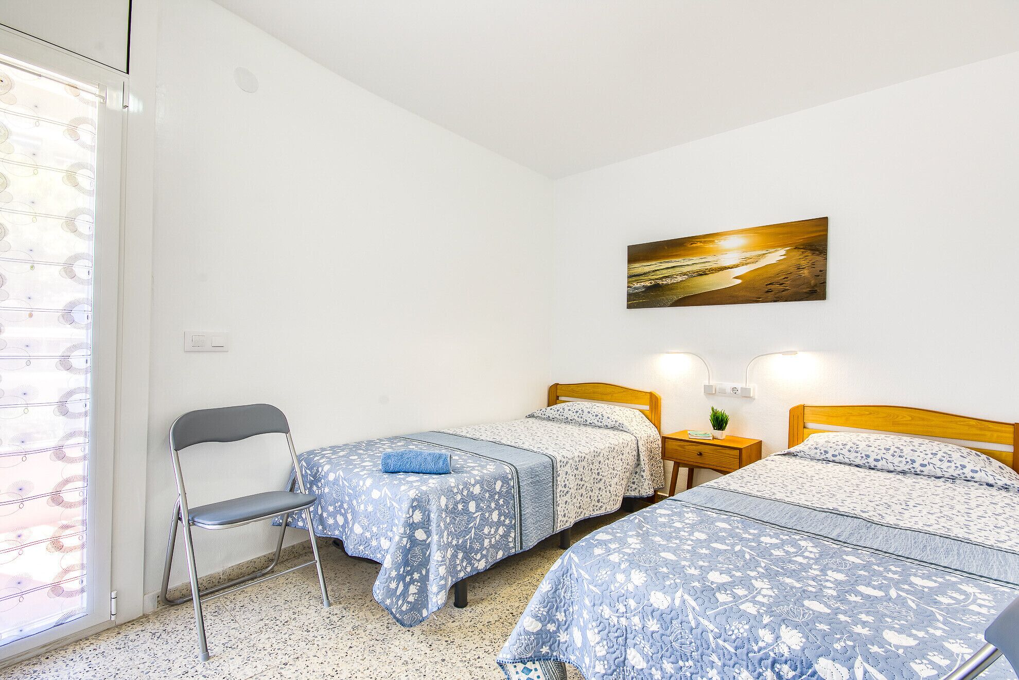 Un dormitorio con dos camas, una silla, una mesita y un cuadro colgado en la pared.