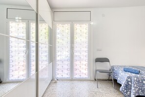 Una stanza con un letto, una sedia e una porta-finestra con tende decorate.