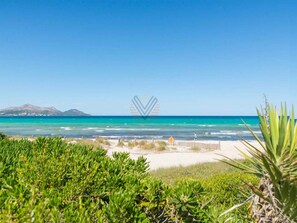 Una playa con aguas turquesas cristalinas, una orilla arenosa y montañas a la distancia.