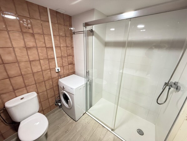 Un baño moderno con inodoro, lavadora y cabina de ducha de vidrio.