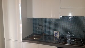 A kitchen with white cabinets, a stainless steel sink, a gas stove, and blue-tiled backsplash. - villas overlooking the sea (Gallina)