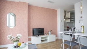 Una cocina moderna con armarios blancos, un área de comedor con mesa y sillas blancas, y un televisor sobre un mueble blanco.