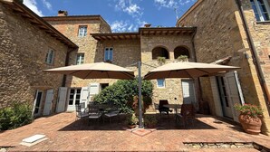A courtyard with stone buildings, two outdoor tables with umbrellas, and potted plants.