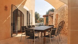 Eine Terrasse im Freien mit Tisch und Stühlen, Steinmauern und einem überdachten Bereich.
