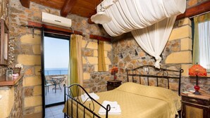 A room with a bed, a stone wall, a balcony, and a view of the sea.