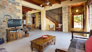 A stone-walled living room with a wooden coffee table, a television, and a staircase leading to another level.
