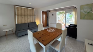Una sala moderna con una mesa de comedor de madera, sillas blancas, un sofá gris y una pequeña mesita auxiliar blanca.