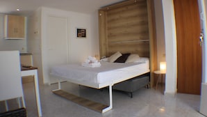 Un dormitorio con cabecera de madera, una cama con ropa de cama blanca, una mesita de noche con una lámpara y un escritorio pequeño con una silla.