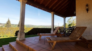 Un espacio de estar al aire libre con techo, con vista a un jardín ajardinado y colinas distantes.