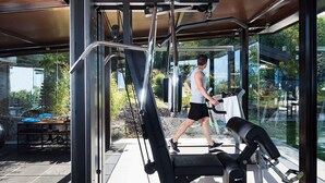 Un gimnasio al aire libre con equipo de ejercicio, un área techada y vistas del jardín y árboles circundantes.