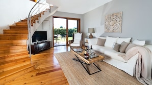 Una sala de estar moderna con una escalera de madera, un sofá blanco, una mesa de centro y un televisor.