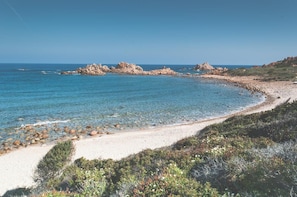 Un paysage côtier caractérisé par une eau d’un bleu limpide, une plage de sable et des affleurements rocheux.