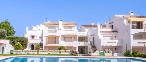 A poolside view of a resort with white buildings, balconies, and a clear blue sky.