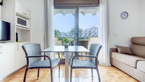 A modern apartment with a balcony, a dining area with wicker chairs, a sofa, and a TV. - JARDINS I 22 Roses (Rosas / Roses)