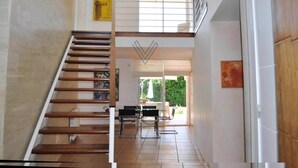 Ein modernes Interieur mit einer Holztreppe, die zu einer zweiten Etage führt, einem Essbereich mit Tisch und Stühlen sowie Blick auf Grünflächen außen.